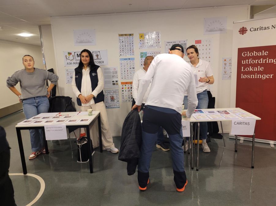 en gruppe mennesker som står i et rom med bord og stoler