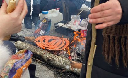 En person som holder en pinne over et bålsted med en pizza på