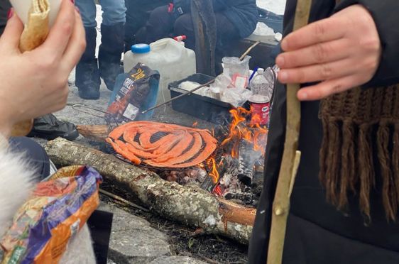En person som holder en pinne over et bålsted med en pizza på