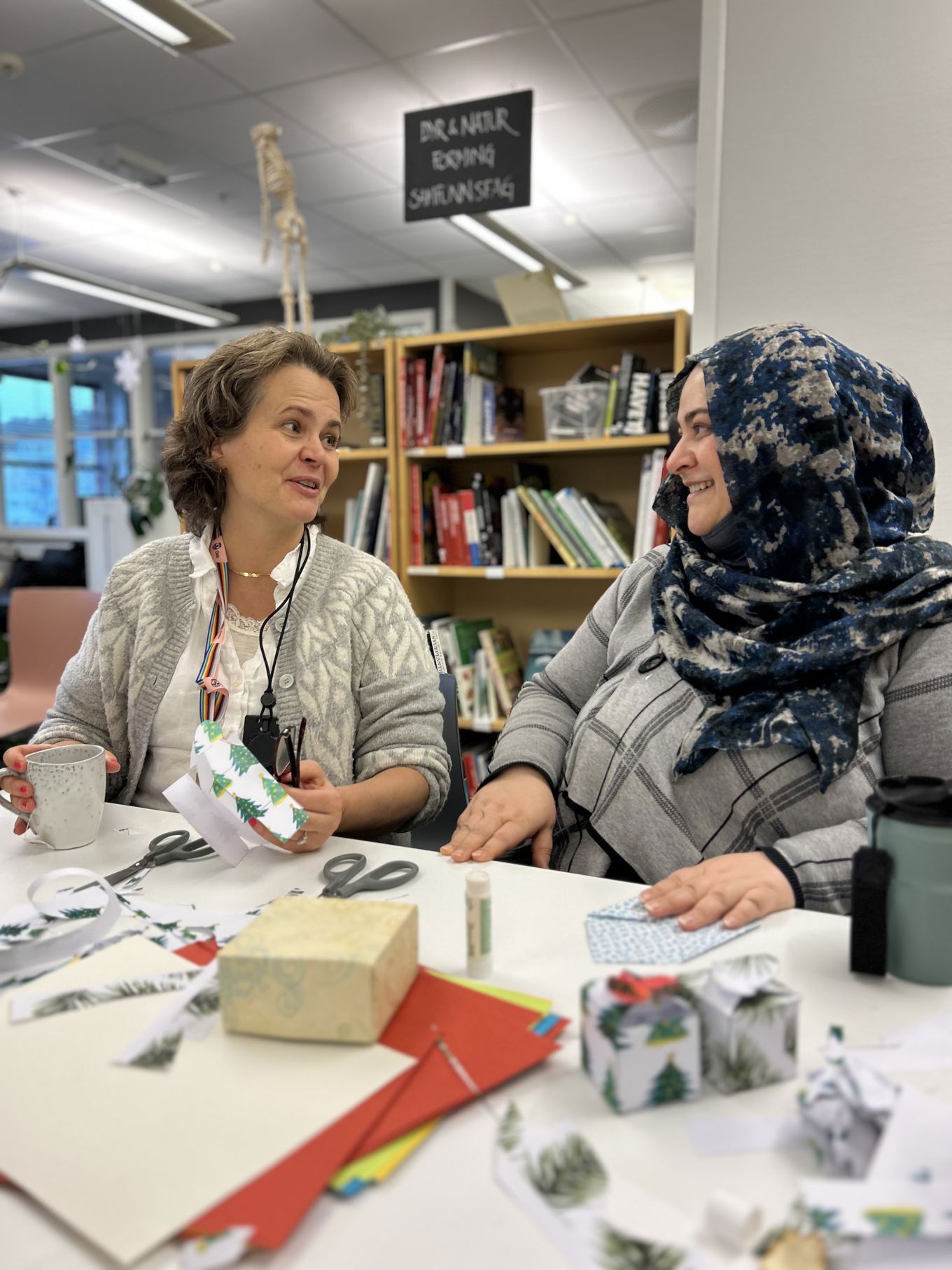 Foto: Marita et par personr som sitter ved et bord med bøker og en bok